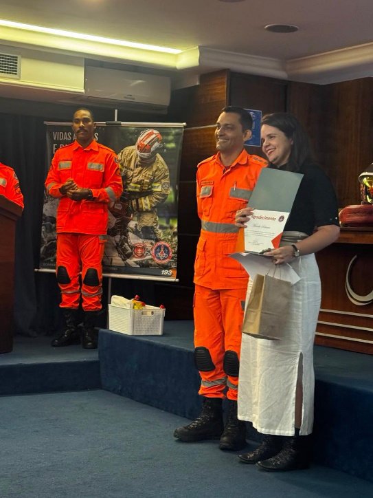 Lorena Lima recebendo certificado de reconhecimento de um bombeiro militar no palco do seminário.